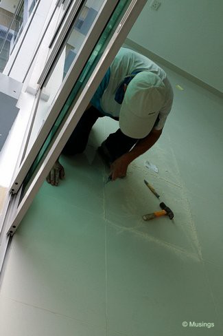 Two of our living room homogenous tiles had long and wide visible scratches on them. A worker is outlining the edges of both tiles in preparation for them to be chiseled away.