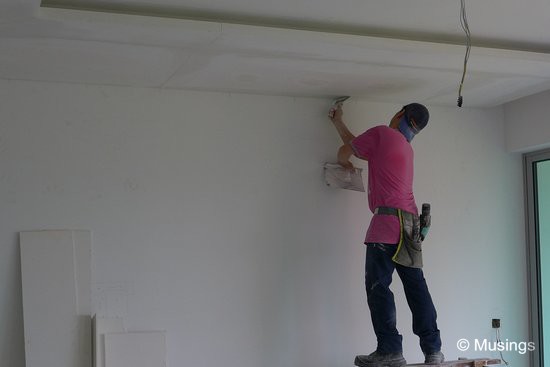 A worker who is wearing a reverse-cap means business! The ceiling boards' surfaces are not perfectly smooth, so they are layered over to get them ready for painting.
